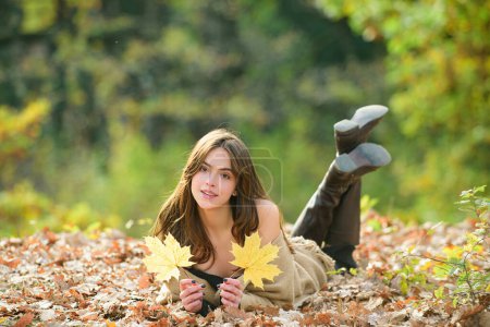 Téléchargez les photos : Souriant portrait de fille heureuse, couché dans les feuilles d'automne. En plein air. Humeur d'automne. Jeune femme profitant du beau temps - en image libre de droit