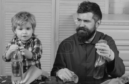 Téléchargez les photos : Papa et gamin s'amusent pendant le nettoyage. Un homme avec un enfant joue avec des savons. Père enseigne un nettoyage à un fils. L'homme accoutume le garçon à la propreté - en image libre de droit