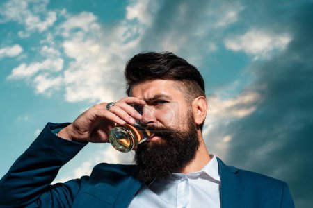 Téléchargez les photos : Gros plan d'un bel homme barbu élégant dégustant du brandy ou du whisky - en image libre de droit