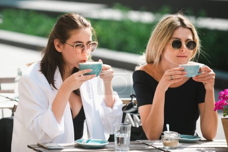 Téléchargez les photos : Deux belles filles avec des tasses de café dans le café d'été. Filles amies dans le café en plein air. Portrait en plein air de deux jeunes belles femmes amies buvant du café - en image libre de droit
