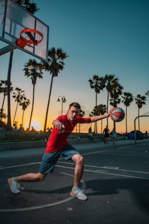 Téléchargez les photos : Hommes sportifs jouant au basket-ball en plein air par une journée ensoleillée au lever du soleil - en image libre de droit