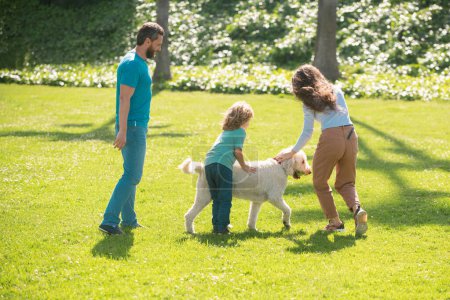 Foto de Madre, padre e hijo están corriendo con el perro en el parque. Feliz familia joven pasar tiempo juntos fuera en la naturaleza verde. Lindo retrato familiar - Imagen libre de derechos