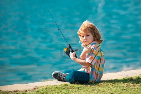 Téléchargez les photos : Pêche d'enfant sur le lac. Jeune pêcheur. Garçon avec fileuse à la rivière. Portrait de garçon excité pêche. Garçon à la jetée avec tige. Concept de pêche - en image libre de droit