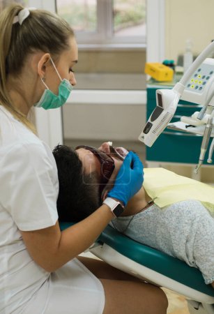 Téléchargez les photos : Jeune homme choisissant la couleur des dents chez le dentiste, gros plan. Homme barbu ayant des dents examinées chez les dentistes. Homme âgé ayant un traitement dentaire au cabinet des dentistes. Soins dentaires et blanchiment des dents - en image libre de droit