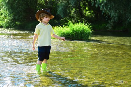 Foto de Niño pescando en un río del bosque. Niño de camisa amarilla con caña de pescar junto al río. Niños pescando. Pescador con sombrero - Imagen libre de derechos