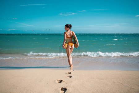 Foto de Female buttocks in thongs bikini, sexy ass. Young woman holding a pineapple on sea sand beach background - Imagen libre de derechos