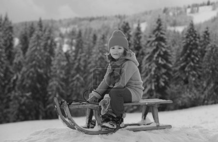 Téléchargez les photos : Joli garçon profitant d'une balade en traîneau. Luge d'enfants, équitation d'un jeu de luge à l'extérieur dans la neige sur le paysage hivernal. Amusement actif d'hiver extérieur pour des vacances en famille - en image libre de droit