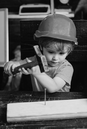 Photo for Child with helmet in orange hard hat. Tools construction. Boy hammering. Kid hammers nail - Royalty Free Image