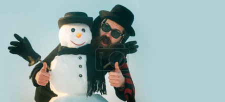 Téléchargez les photos : Joyeux Noël et bonne année. Humour hiver bonhomme de neige en chapeau jouer avec bonhomme de neige en plein air. Homme avec bonhomme de neige sur fond d'hiver. Bonhomme de neige pour bannière d'hiver - en image libre de droit