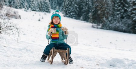 Foto de Chico divertido divirtiéndose con un trineo en invierno. Lindo juego de niños en una nieve. Actividades de invierno para niños - Imagen libre de derechos