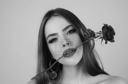 Foto de Closeup fresh face girl. Brunette woman with red rose. Beautiful girl with reses flowers. Closeup face of young beautiful woman with a healthy clean skin and bright makeup - Imagen libre de derechos