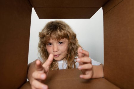 Photo for The surprised child age 8 year unpacking, opening carton box and looking inside. The package, delivery, surprise, kids gift concept. Parcels, delivery service - Royalty Free Image