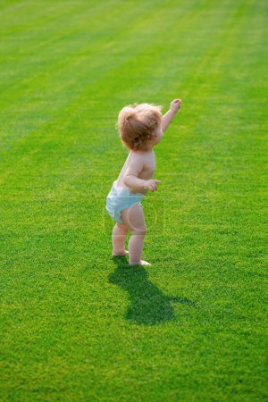 Foto de Bebé en el hermoso campo verde de primavera. Tibia primavera en el parque en pantalones de pañal - Imagen libre de derechos