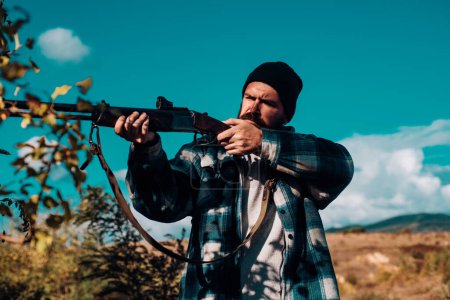Foto de Hombre cazador barbudo sosteniendo arma y caminando en el bosque. Hunter con escopeta a la caza. Gran juego - Imagen libre de derechos