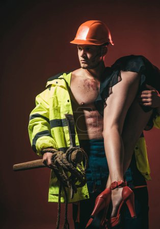 Téléchargez les photos : Dominant dans le jeu de rôle sexuel préliminaires. pompiers sexy corps muscle homme tenant sauvé femme sexy. Concept des professions à risque. Pompier - Chaud et sexy - en image libre de droit