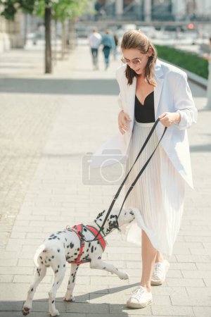 Téléchargez les photos : Femme jouer avec chien, style de rue. Modèle de mode dans la rue de la ville. Mode tenue urbaine. Style vestimentaire quotidien décontracté - en image libre de droit