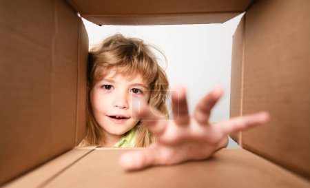 Téléchargez les photos : Kid déballer et ouvrir la boîte en carton, et regarder à l'intérieur avec un visage surprise. Boîte ouverte et colis de livraison pour enfants - en image libre de droit