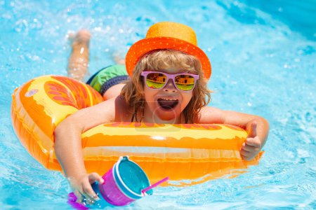 Téléchargez les photos : Portrait d'enfants d'été dans l'eau de mer sur la plage. Cocktail d'été pour enfants. Joyeux petit garçon avec anneau gonflable coloré dans la piscine extérieure le jour d'été chaud - en image libre de droit