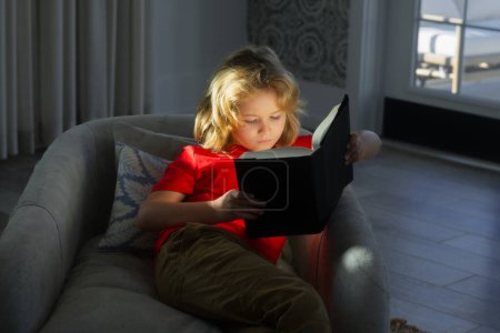 Photo for Portrait of cute blonde child reading interesting kids book story. Kids and literature. Child reading book, sitting at home in cozy living room on couch - Royalty Free Image