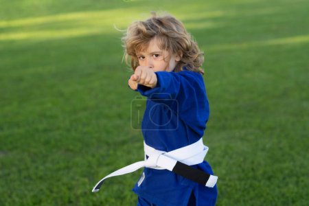 Foto de Niño practicando karate al aire libre. Niños de karate deportivo. Un niño usando kimono haciendo karate en el parque. Niño con deporte de entrenamiento. Pequeño luchador de karate. Artes marciales para niños. Niño en kimono - Imagen libre de derechos