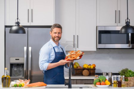 Photo for Portrait of happy smiling man in cook apron preparing fresh natural meal salmon at kitchen. Handsome cheerful chef man in chef apron preparing raw fish salmon. Healthy food, cooking concept - Royalty Free Image