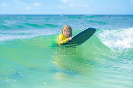 Photo for Kid little surfer learn to ride on surfboard on sea waves. Happy child playing in the sea. Kid having fun at the beach. Surfer child is riding a wave. Kid learning to surf in sea or ocean - Royalty Free Image
