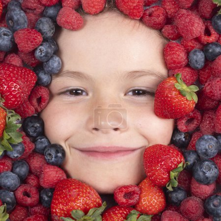 Téléchargez les photos : Vitamines de berrie. Visage d'enfant avec cadre de baies, fermer. Les baies mélangent myrtille, framboise, fraise, mûre. Mélange assorti de fraise, myrtille, framboise, mûre près du visage de l'enfant - en image libre de droit