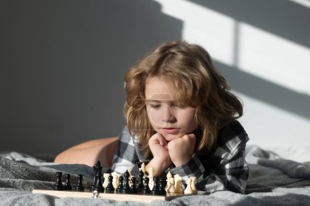 Téléchargez les photos : Jeu d'échecs avec des enfants à la maison. Un gamin qui joue aux échecs. Enfant pensant à l'échiquier. Apprendre et grandir des enfants, bien-être des enfants. Développement précoce des enfants - en image libre de droit