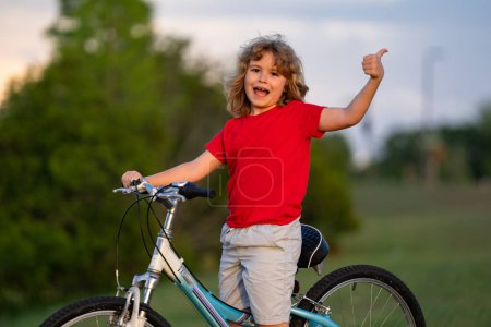 Foto de Niño pequeño montando en bicicleta en el parque de verano. Un niño conduce una bicicleta en un camino de entrada afuera. Chico montando bicicletas en la ciudad. Niño en bicicleta al aire libre. Bicicleta para niños en el vecindario americano - Imagen libre de derechos