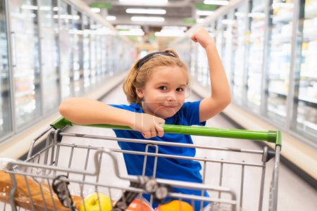 Photo for Kid with shopping cart at grocery store. Shopping in supermarket. Kids buying groceries in supermarket. Little boy buy fresh vegetable in grocery store. Child buy food - Royalty Free Image