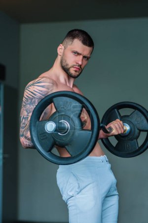 Photo for Muscular hunk with posing in gym. Fitness male model near gym equipment. Young muscular man workout. Sport man with strong muscular torso in gym. Sport and motivation. Exercises with weight - Royalty Free Image
