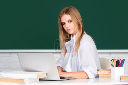 Téléchargez les photos : Jeune étudiante avec ordinateur portable dans une salle de classe universitaire. Étudiante en uniforme. étudier en classe. Étudiant au tableau noir. Étudiante sur le bureau. Journée des étudiants. Retour à l'école - en image libre de droit