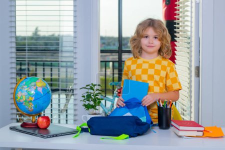 Photo for School kid 7-8 years old puts school supplies in a backpack. Preparation for school. Little student learning and doing homework. Education at home concept - Royalty Free Image