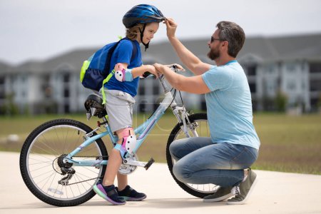 Photo for Father and son riding bike in park. Child in safety helmet with father riding bike in summer day. Father teaching son riding bike. Father helping son to wear a cycling helmet. Child in safety helmet - Royalty Free Image