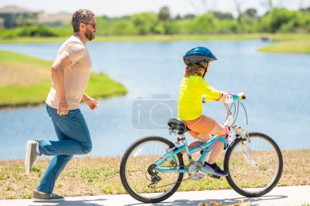 Photo for Sporty family father and son riding bike on a park. Child in safety helmet riding bike on summer day. Father teaching son riding on bike. Child son in bike helmet on bicycle. Fatherhood, Fathers day - Royalty Free Image