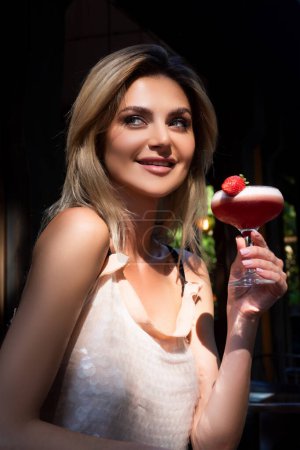 Photo for Cocktail party concept. Sensual woman wearing a white cocktail dress drinking a tropical cocktail decorated with decorated with strawberry - Royalty Free Image