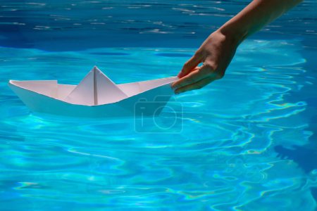Photo for Female hand holding paper boat on the sea background. Tourism and traveling, travel dreams vacation holiday, sailing adventure. Origami paper boat sailing on water causing waves and ripples - Royalty Free Image