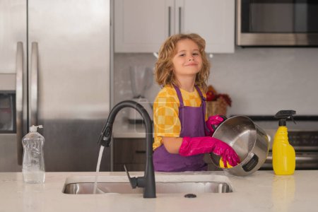 Photo for Dish washing concept. Child washing dishes in the kitchen interior. Child helping his parents with housework. Housekeeping and home cleaning concept. Child use duster and gloves for cleaning - Royalty Free Image