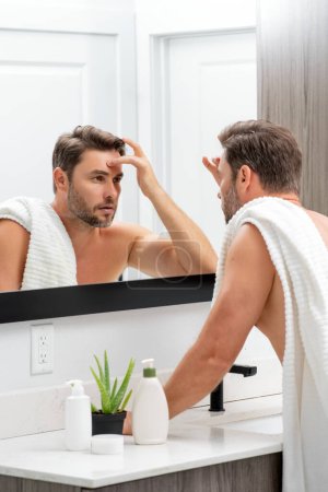 Photo for Millennial hispanic man looking in mirror, facial skin and stubble. Male beauty care product. Skincare, home spa. Beauty portrait of a beautiful man. Spa model, moisturizing nourishing creme - Royalty Free Image