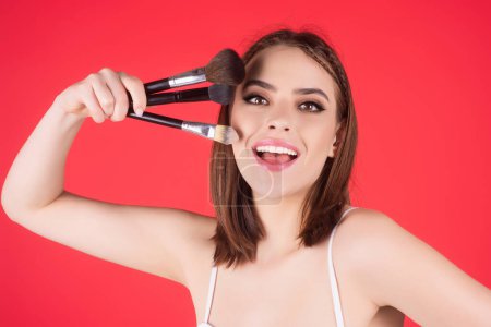 Téléchargez les photos : Young woman applies powder on the face using makeup brush. Beautiful girl doing contouring apply blush on cheeks. Face beauty cosmetics. Fresh skin and natural make up. Powder blush on facial skin - en image libre de droit