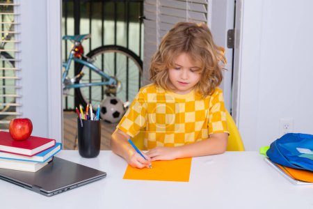 Téléchargez les photos : Concept scolaire et éducatif. Portrait d'enfant mignon écolier assis à la table écrivant des devoirs scolaires à la maison. Retour à l'école - en image libre de droit