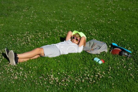 Foto de Niña descansando sobre hierba verde. Los niños felices descansan al aire libre. Niños relajándose en el parque de primavera. Niño acostado sobre hierba verde - Imagen libre de derechos