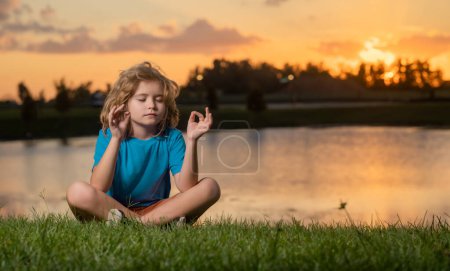 Téléchargez les photos : Enfant calme et se détendre sur fond de nature. Petit enfant médite tout en pratiquant le yoga. Liberté et concept insouciant. En plein air méditant au coucher du soleil d'été - en image libre de droit
