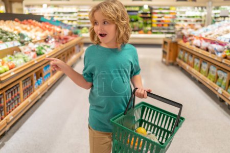 Téléchargez les photos : Enfant avec panier. Enfant qui choisit de la nourriture dans une épicerie ou un supermarché. Fruits et légumes - en image libre de droit