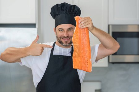 Téléchargez les photos : Cuisinière homme chef tenir du saumon de poisson. Chef masculin en uniforme de chef avec filet de saumon de poisson cru. Chef homme cuisine poisson filet de saumon sur la cuisine - en image libre de droit