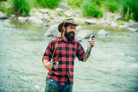 Téléchargez les photos : Pêcheur utilisant la canne à pêche dans la rivière de montagne. Un pêcheur à la mouche pêche la truite sauvage sur la rivière dans la forêt. Pêcheur homme dans l'eau attraper des poissons - en image libre de droit