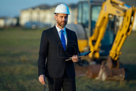 Photo for Construction builder investor. Man investor in front of construction site. Successful handsome man standing at modern home building construction. Portrait of midlle aged investor in suit and helmet - Royalty Free Image