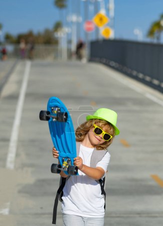 Téléchargez les photos : Enfant skateboarder dans le skate park. Petit garçon avec skateboard. Enfance, loisirs, concept de style de vie. Portrait élégant enfant avec planche à roulettes en plein air - en image libre de droit