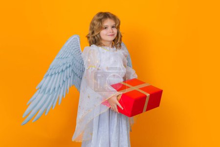 Téléchargez les photos : Angel child hold gift present. Valentines day. Blonde cute child with angel wings on a yellow studio background. Happy angel child - en image libre de droit