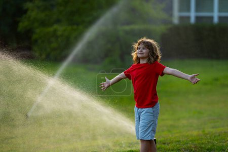 Photo for Child play near automatic sprayers in the garden. Watering in the garden. Kid freshness of nature. Automatic lawn sprinkler watering grass. Garden irrigation system watering lawn. Sprinkler system - Royalty Free Image